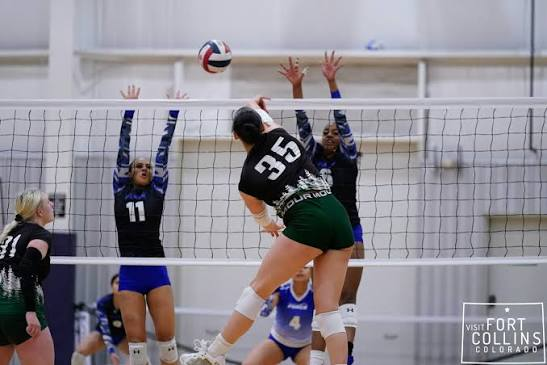 Colorado volleyball player in green swinging over a two-player block during a match in Fort Collins