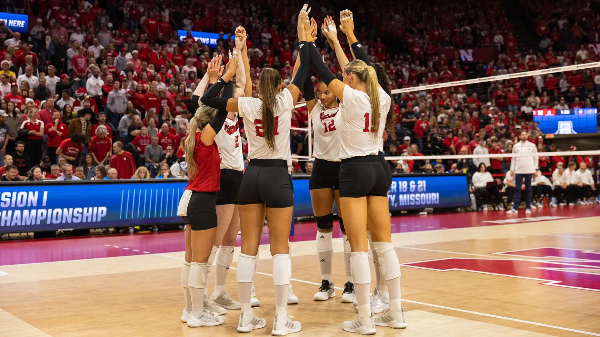 Nebraska volleyball team huddling at the net before a 2026 schedule match in front of a sold-out red crowd