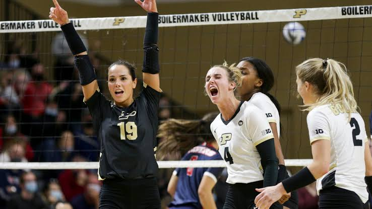 Purdue volleyball players cheering in front of the Boilermaker Volleyball banner during a Big Ten home match