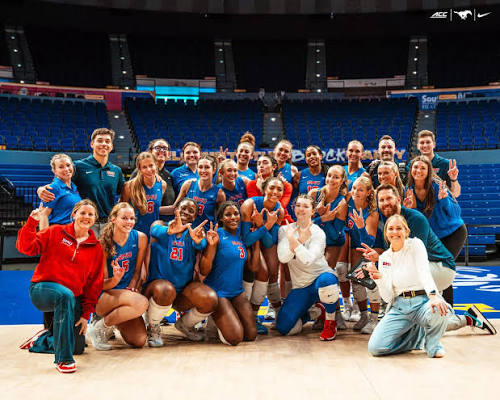 SMU volleyball team and coaching staff posing together on court after an ACC road win