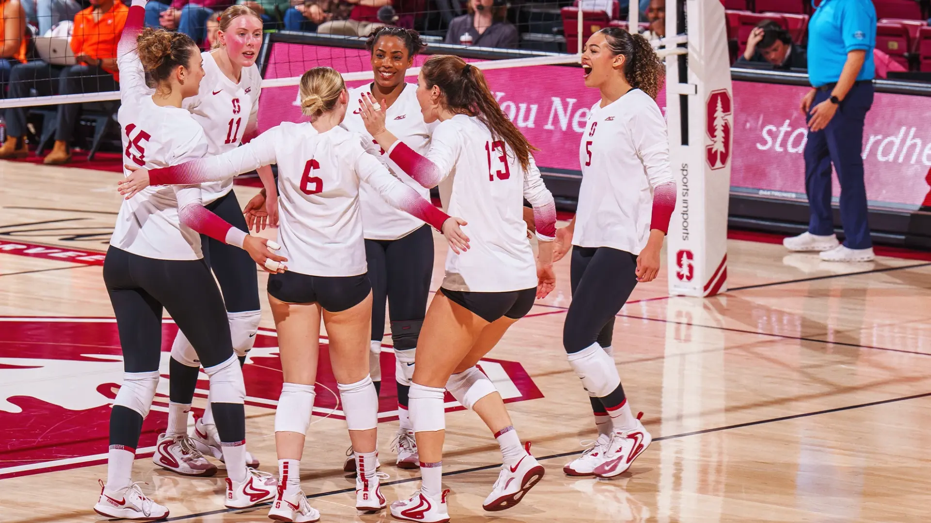 Stanford Cardinal volleyball team huddling at the net after winning a rally at Maples Pavilion