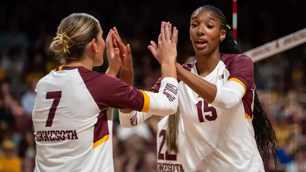 Minnesota volleyball teammates high-fiving in maroon and gold jerseys after winning a point in a Big Ten match