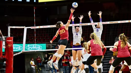 Iowa State volleyball player number 20 attacking against a double block at Hilton Coliseum