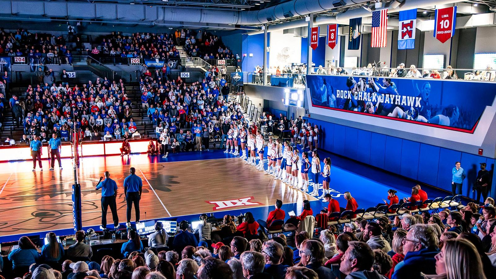 Kansas volleyball team lined up for introductions at Horejsi Family Volleyball Arena under the Rock Chalk Jayhawk banner