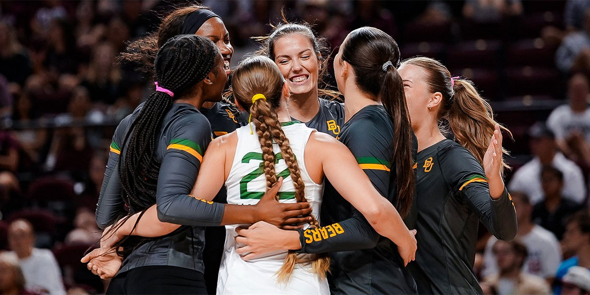 Baylor Bears volleyball teammates hugging in a celebration huddle during a 2026 Big 12 road match