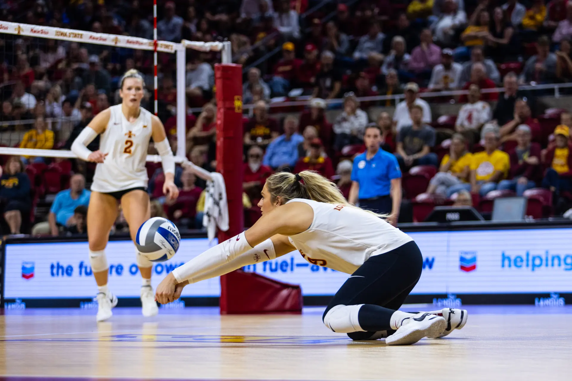 Iowa State volleyball defender dropping low for a dig in front of a packed Hilton Coliseum crowd