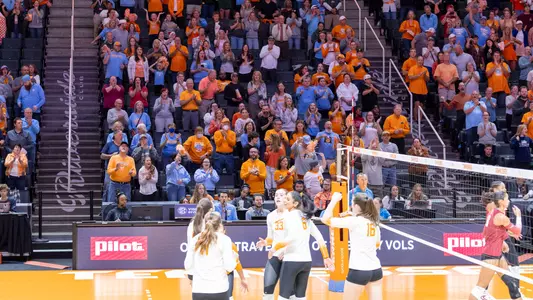 Tennessee volleyball players huddling as a packed orange-clad Thompson-Boling Arena crowd cheers during a 2026 home match