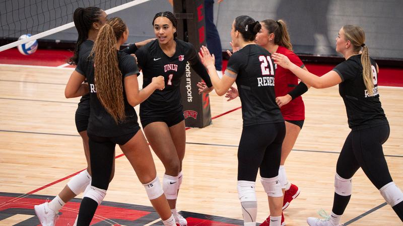UNLV volleyball players in black Rebels jerseys celebrating a point together on the court