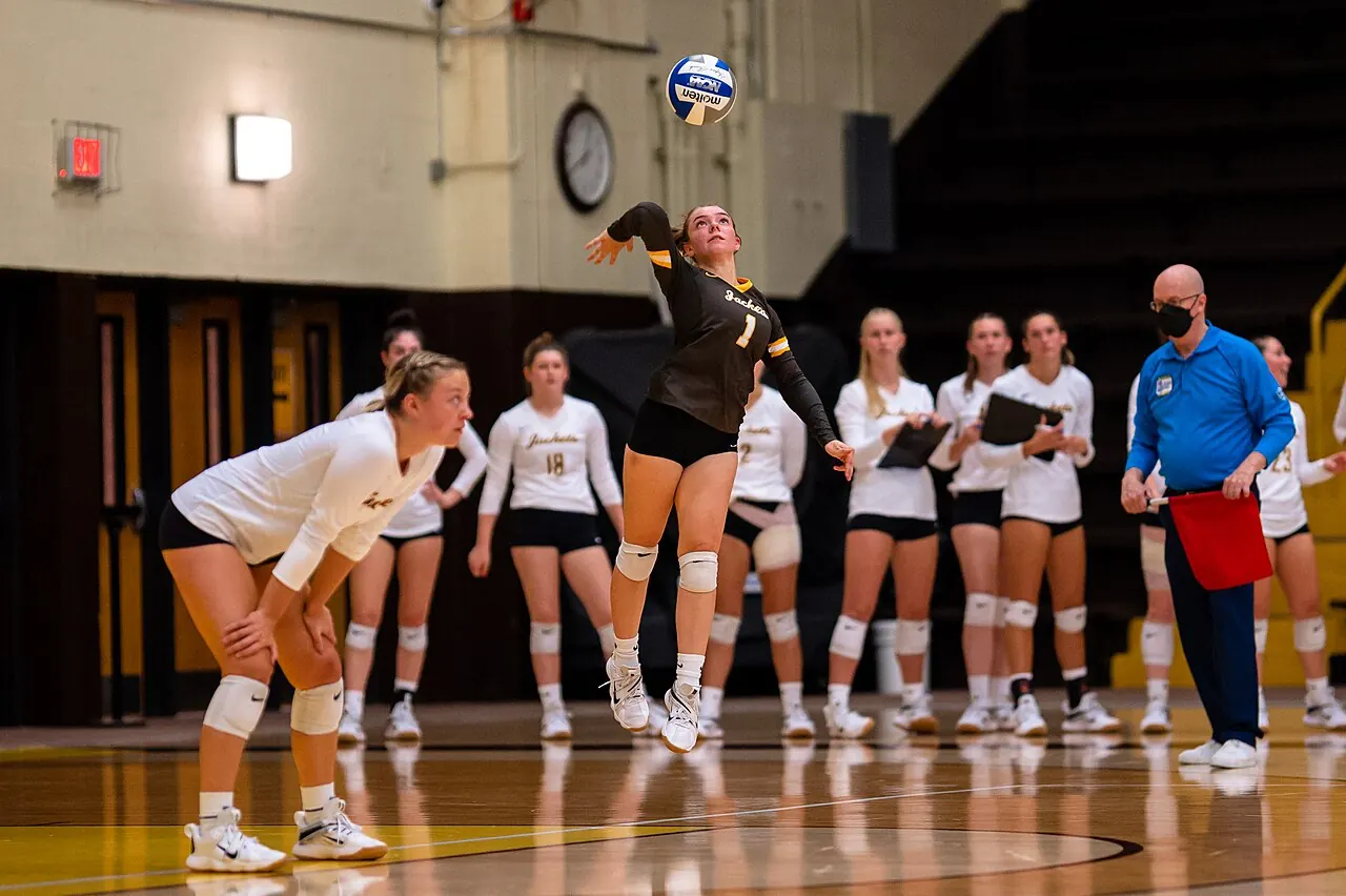 A Baldwin Wallace volleyball player in a black uniform raising one arm as the ball rises overhead.