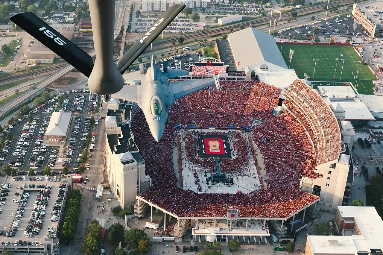 Aerial view of a volleyball court and packed stands at Nebraska’s Memorial Stadium during a military flyover.