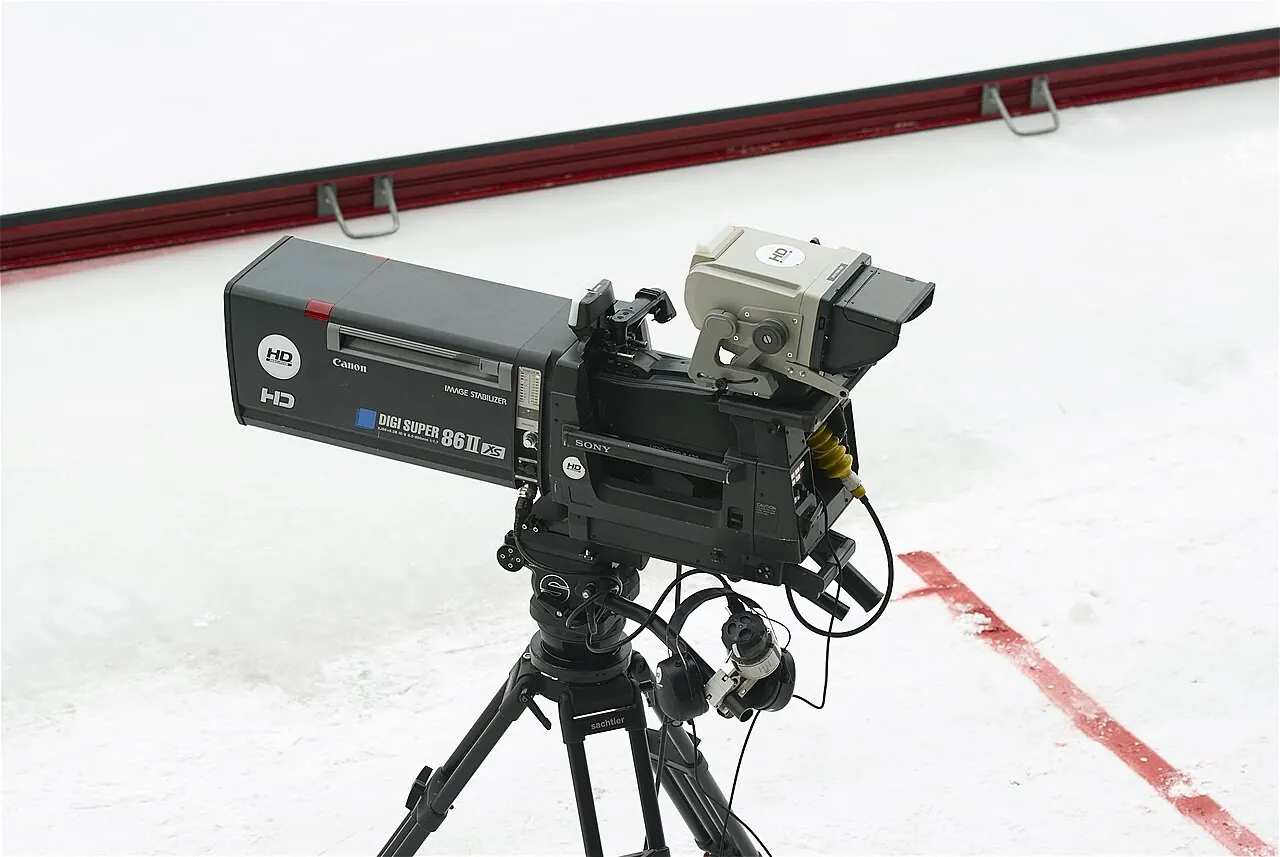 A professional Sony television camera with a large Canon broadcast lens beside a sports playing area.