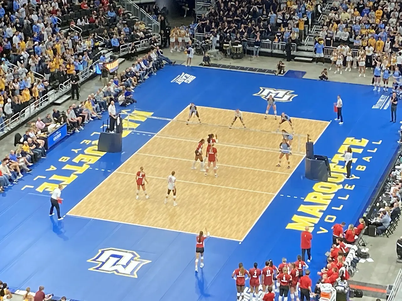Wisconsin and Marquette players moving into position around the net during a volleyball rally.