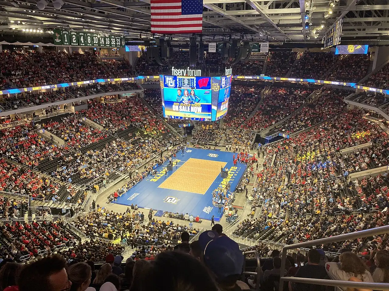 Wide view of the volleyball court and crowded Fiserv Forum stands during a timeout.