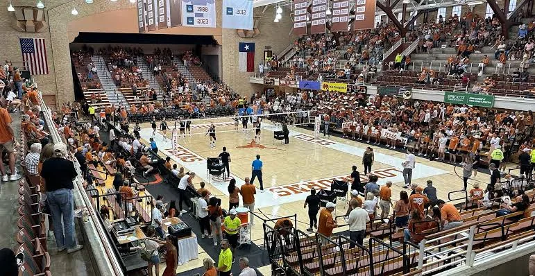 Volleyball players on the Gregory Gym court with spectators along both sidelines