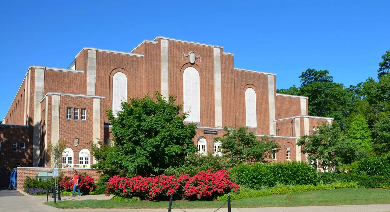 Brick facade and arched windows of the Wisconsin Field House behind trees and flower beds